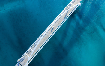 Aerial shot of a white bridge over blue water with a single van crossing the bridge