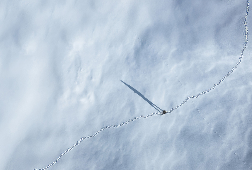 A man walking in the snow and leaving footprints behind him.