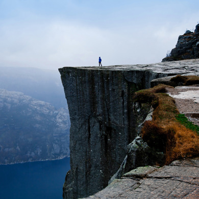 A man at the edge of the cliff with water running at the bottom. 